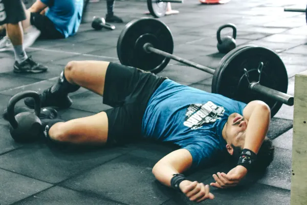 A man in a gym, lying on the floor, exhausted from a workout.